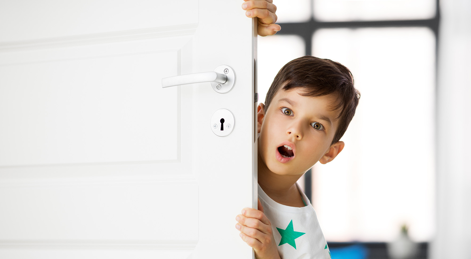 surprised little boy behind door at home